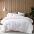 A bed adorned with a textured white comforter set, providing a sophisticated and inviting bedroom atmosphere.