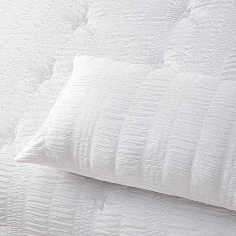 Close up details of a textured white comforter set, providing a sophisticated and inviting bedroom atmosphere.