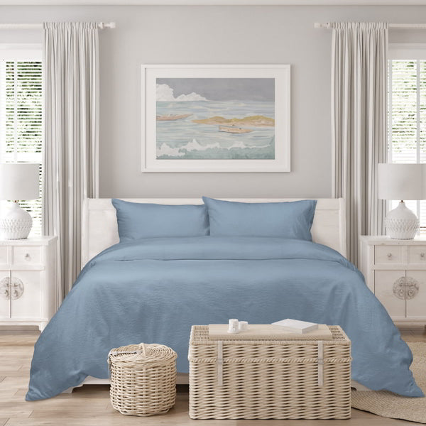 A blue bed with white walls and a white bedside table, showcasing the elegance of the Romy Blue Quilt Cover Set in a serene setting.