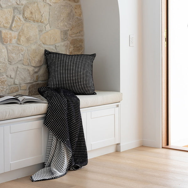 A stylish Dora Black Throw on a bench, showcasing its luxurious waffle fabric and reversible design for versatile decor.