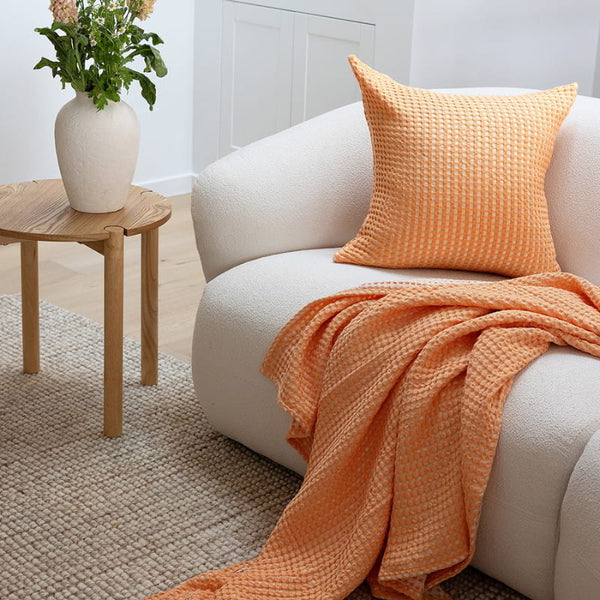 A white couch complemented by the Bambury Dora Peach Throw, featuring a luxurious texture and aesthetic appeal.