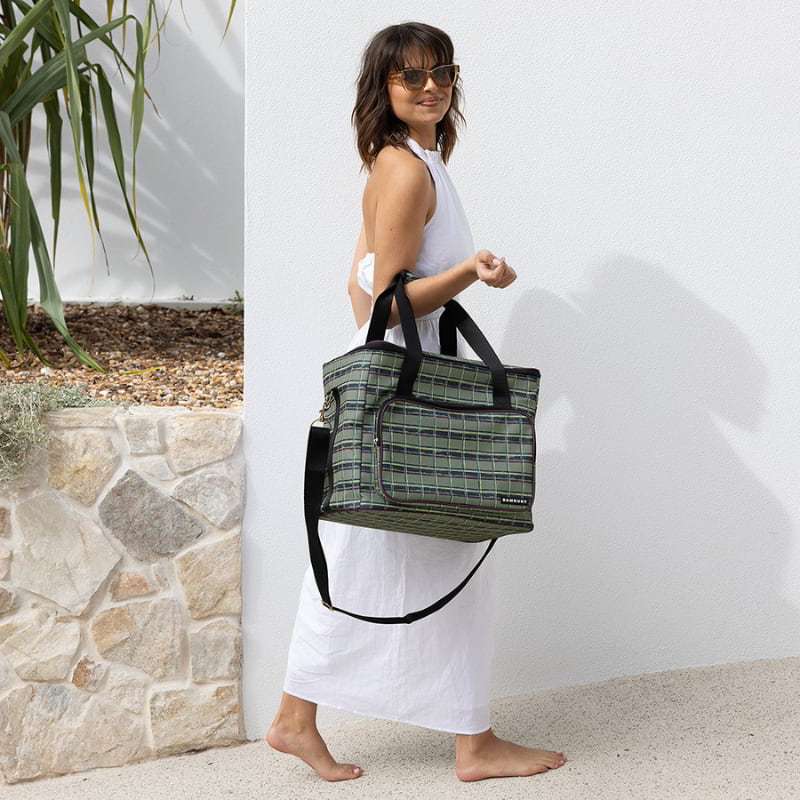 A woman carrying large green cooler bag designed for picnics, featuring a waterproof interior and a zippered front pocket.