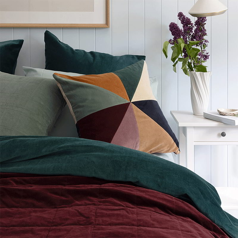 Vibrant multicoloured cushion featuring captivating patchwork design crafted from 100% cotton velvet on a cosy bed.