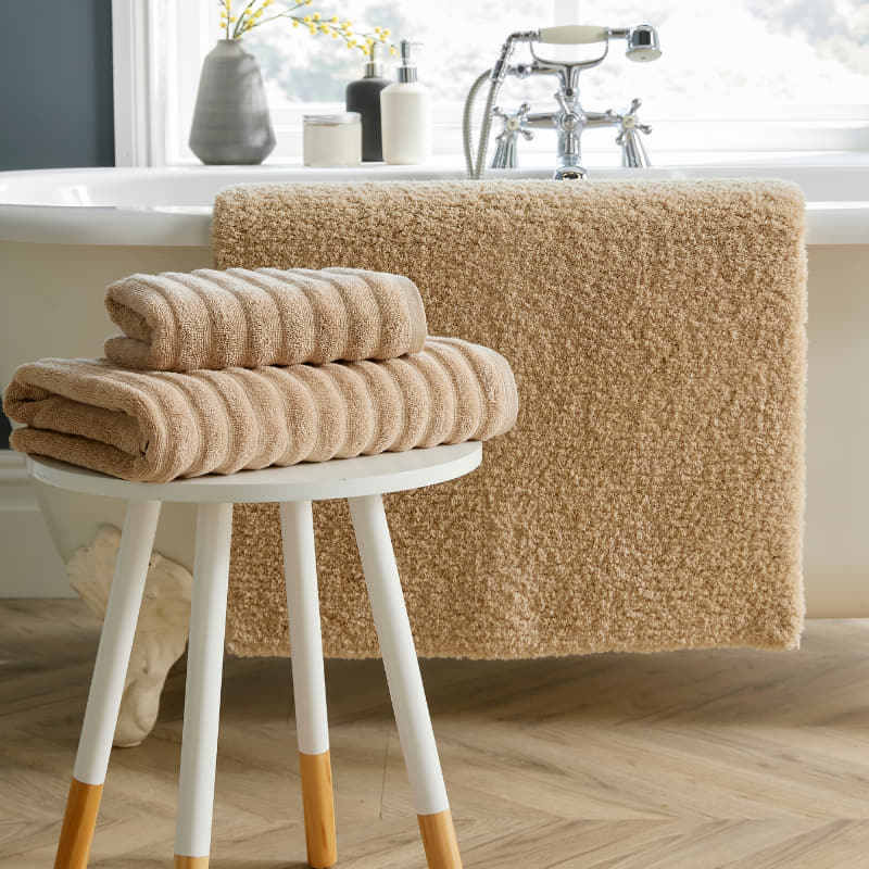 A stylish sand bath mat featuring a stool and towels, contributing to a calming and elegant bathroom setting.