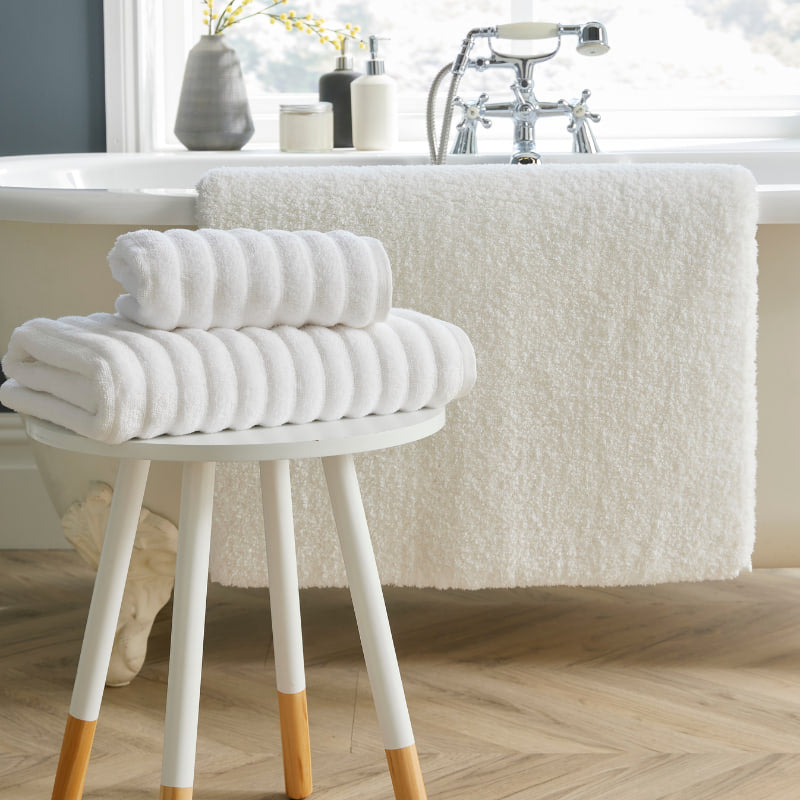 A stylish white bath mat featuring a stool and towels, contributing to a calming and elegant bathroom setting.