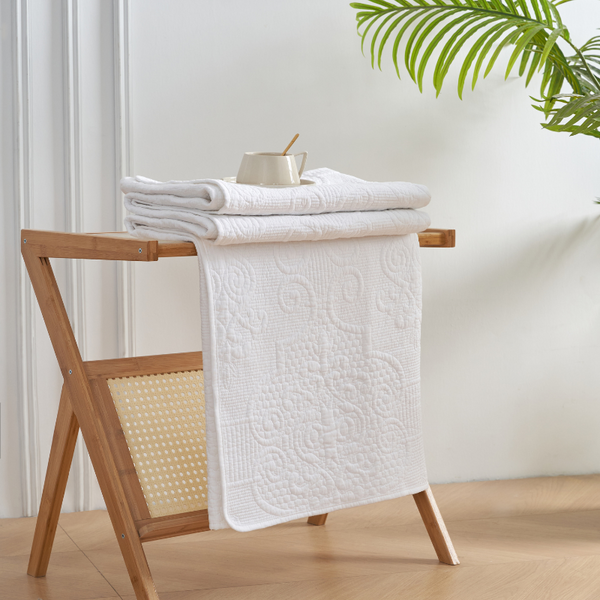 A white throw draped on a wooden stand beside a lush green plant, showcasing a serene and elegant home decor setting.