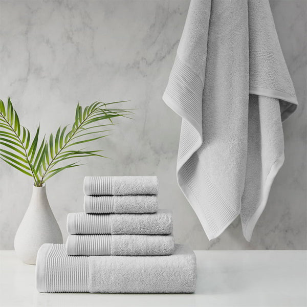 A stack of luxurious grey towels made from eco-friendly materials, placed on a table beside a vibrant green plant.