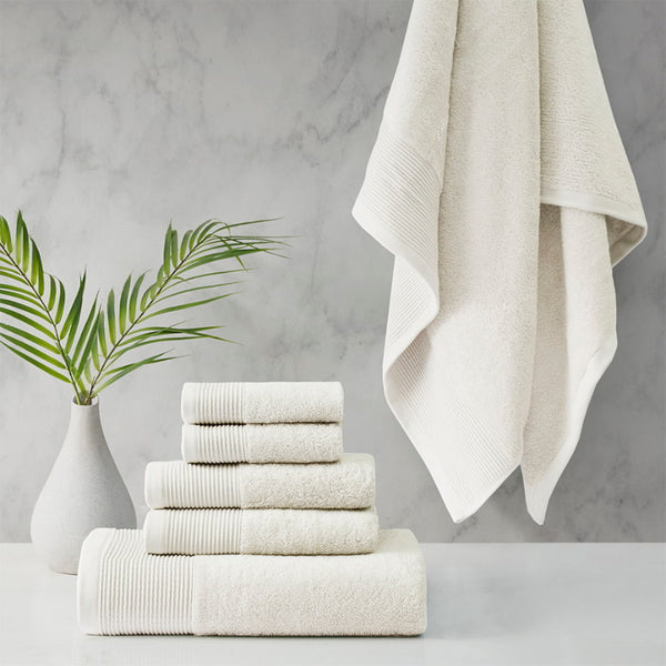 A stack of luxurious ivory towels made from eco-friendly materials, placed on a table beside a vibrant green plant.