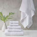 A stack of luxurious white towels made from eco-friendly materials, placed on a table beside a vibrant green plant.