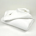 A white blanket is elegantly folded on a white surface, showcasing a minimalist aesthetic and a sense of tranquility.