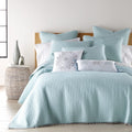 Bright bedroom scene with a light blue comforter and pillows, showcasing playful pom poms for a stylish and comfy vibe.