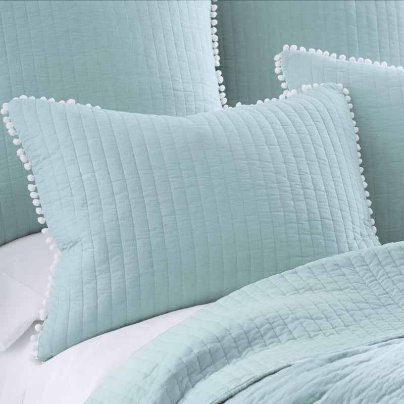 A serene bed setup with blue pillows and a white comforter, highlighted by the cheerful Clavo Pom Pom Coverlet Set.