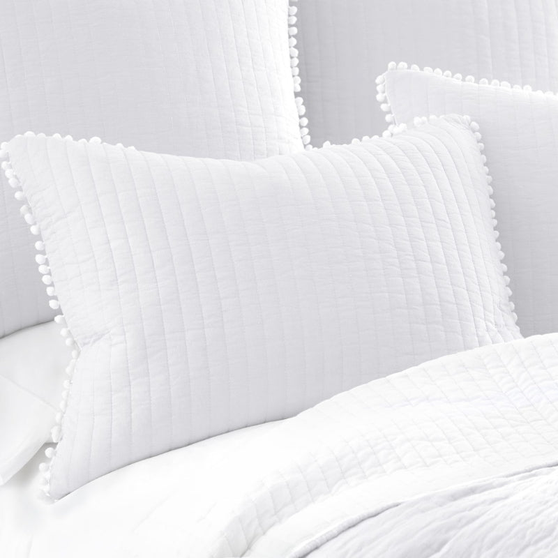 Serene white bed adorned with soft pillows and a quilt, highlighted by l pom-poms for a charming, cozy vibe.