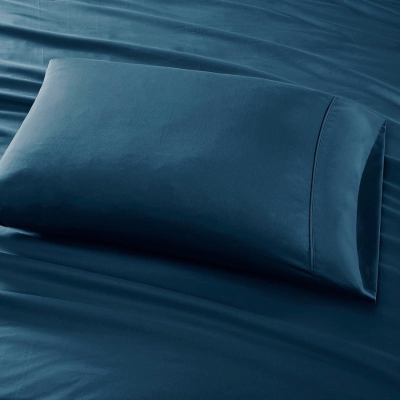 An indigo pillow is placed on a bed, highlighting the elegance of the Park Avenue Egyptian Cotton Sateen Sheet Set.