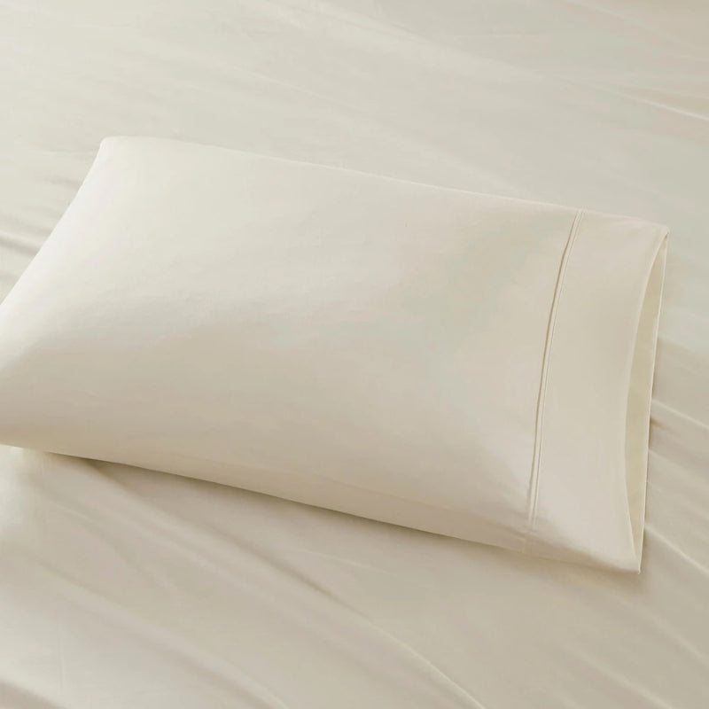 An oatmeal pillow is placed on a bed, highlighting the elegance of the Park Avenue Egyptian Cotton Sateen Sheet Set.