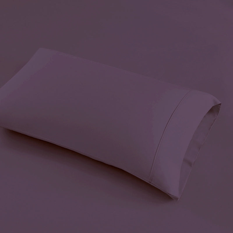 A plum pillow is placed on a bed, highlighting the elegance of the Park Avenue Egyptian Cotton Sateen Sheet Set.