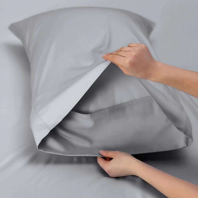 A person inserting a pillow into a dove pillowcase made from soft cotton and TENCEL™ Lyocell for ultimate comfort by Renee Taylor.