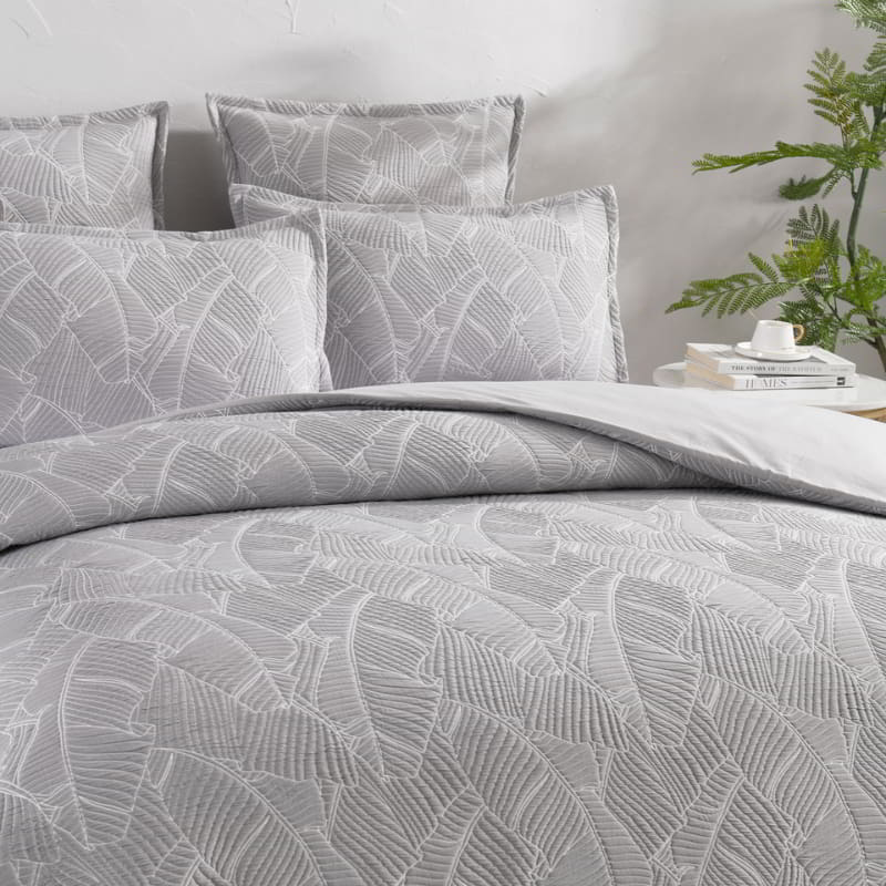 alt="Neutral-toned bedding set, showcasing a tropical banana leaf design, ideal for a rustic retreat."