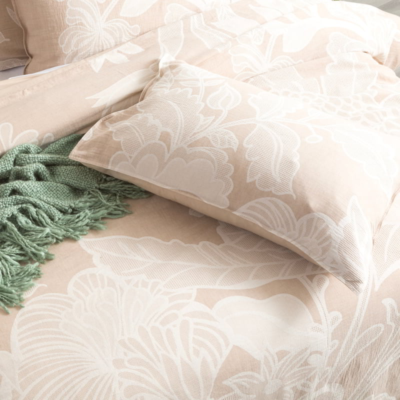 A lavish bed adorned with a white floral pattern and a lush green blanket. The intricately woven pillow adds a touch of elegance.