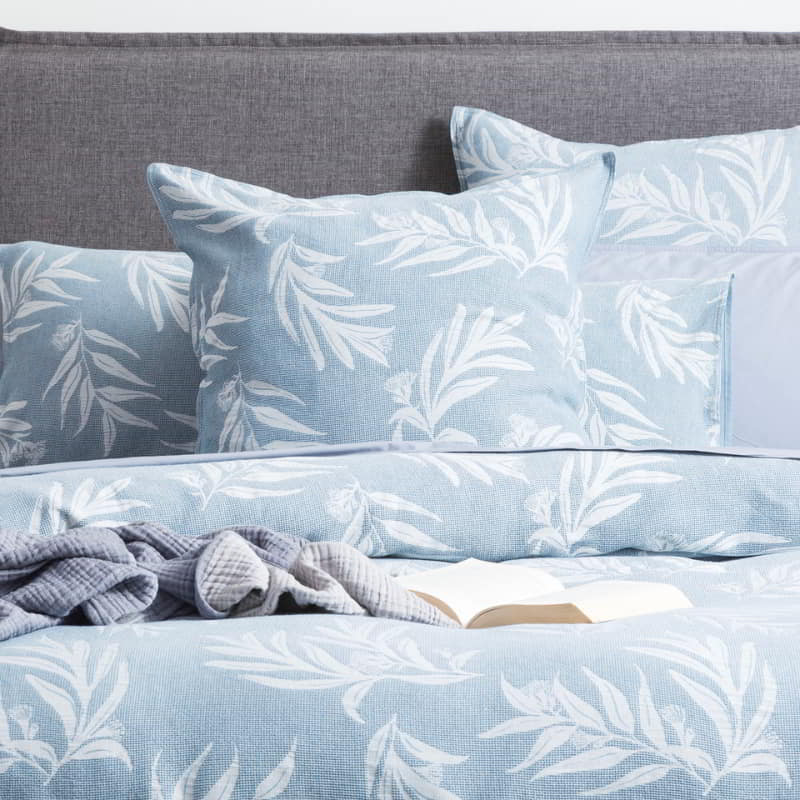 Opulent blue bed with intricate white and blue leaf print, complete with pillows and a French blue quilt cover set adorned with leaf designs.