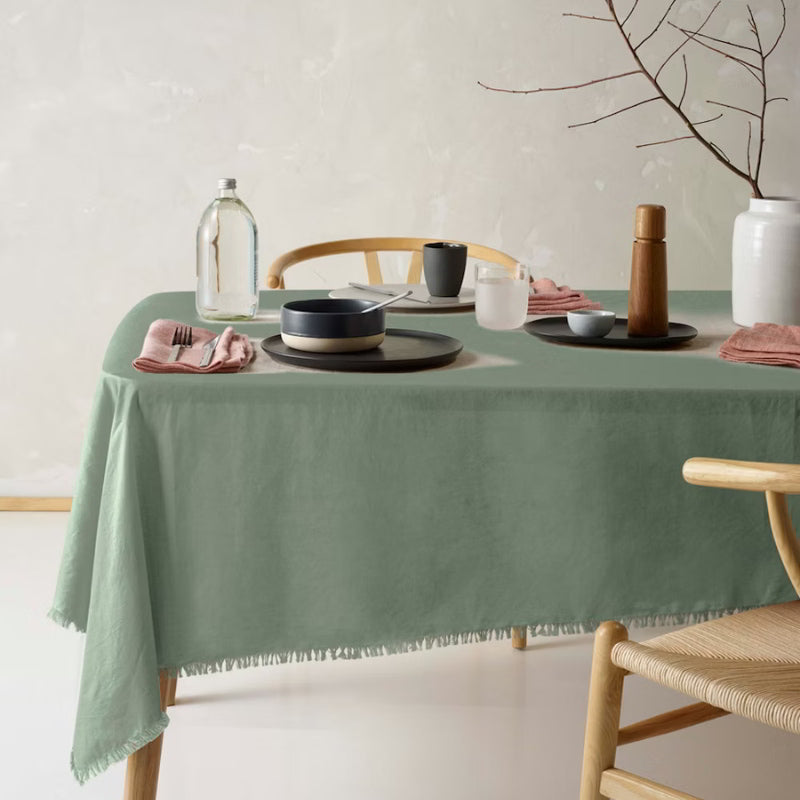 An elegant green tablecloth made of linen and cotton, featuring a soft feel, fringe edges, and a versatile design for any occasion.