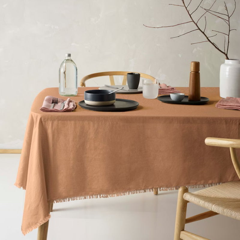 An elegant terracotta tablecloth made of linen and cotton, featuring a soft feel, fringe edges, and a versatile design for any occasion.