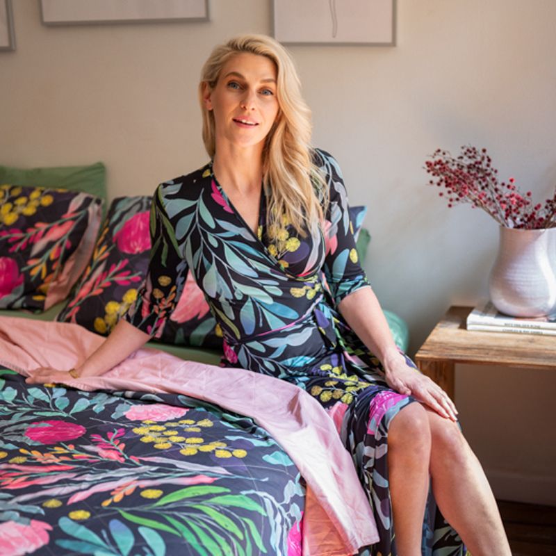 a blonde lady sitting on a floral bed cover on a bed