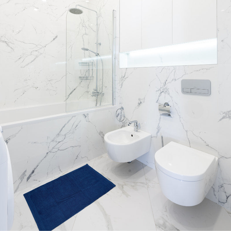 A serene marble bathroom complemented by Jenny Mclean De La Maison Wide Sheared Border Bath Mat for comfort.