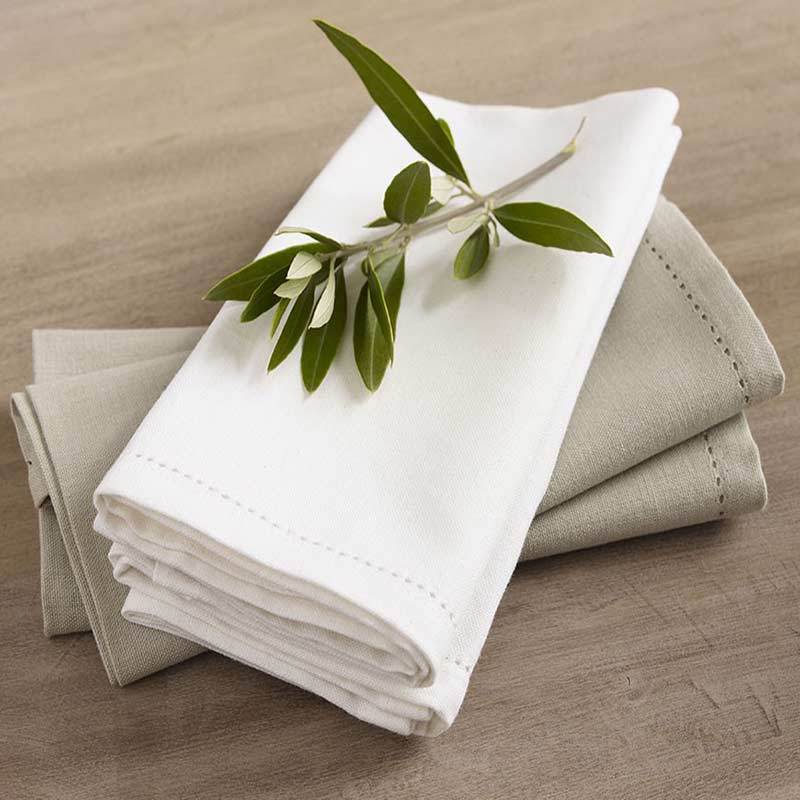 A stack of hemstitch napkins adorned with olive leaves, complementing an elegant dining setup with a classic touch.