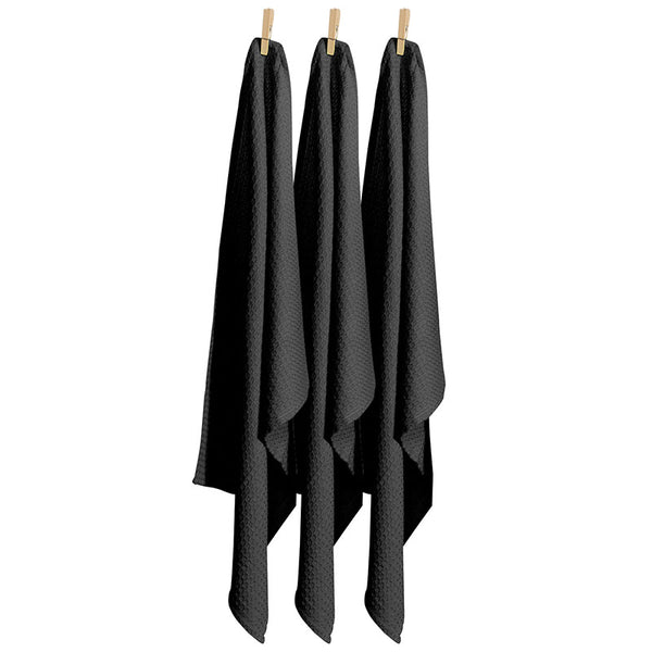 Three black tea towels hanging on clothes pegs, showcasing their vibrant colour and practical design for kitchen use.