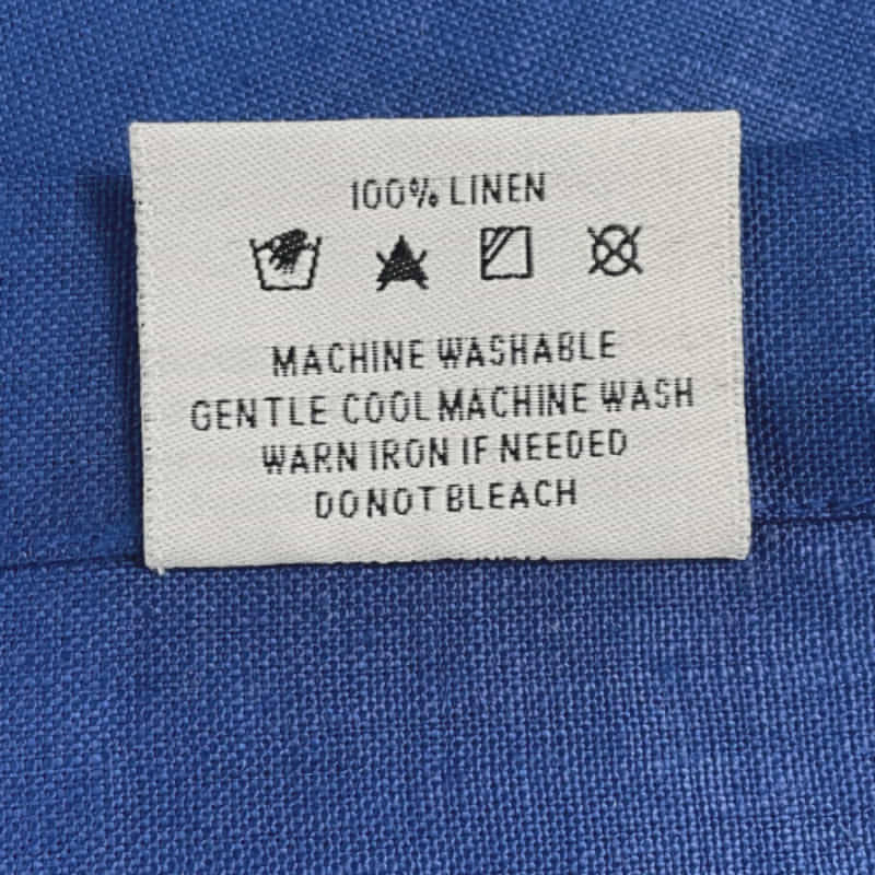 Back tag details on Venice indigo linen napkin, showcasing practicality for effortless garment care.