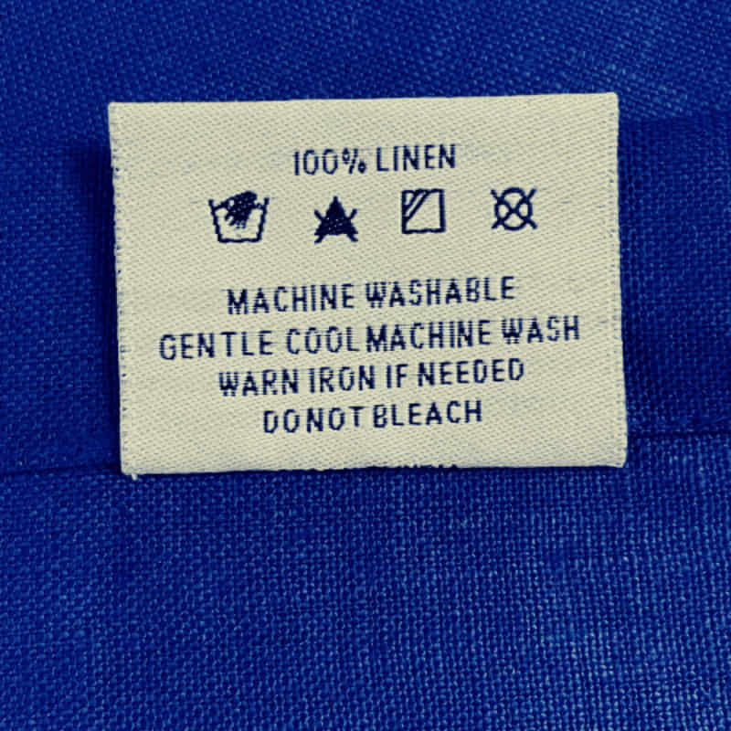 Back tag details of RANS Venice Linen Indigo Tablecloth emphasizing practicality for effortless garment care.