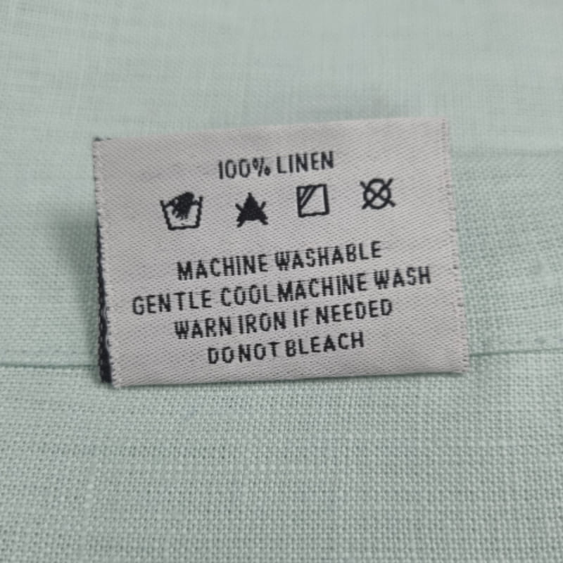 Back tag details on Venice mist linen napkin, showcasing practicality for effortless garment care.