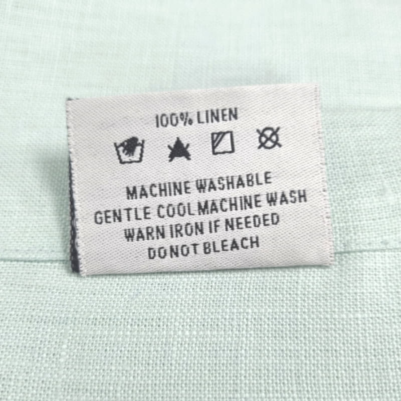 Back tag details of RANS Venice Linen Mist Tablecloth emphasizing practicality for effortless garment care.