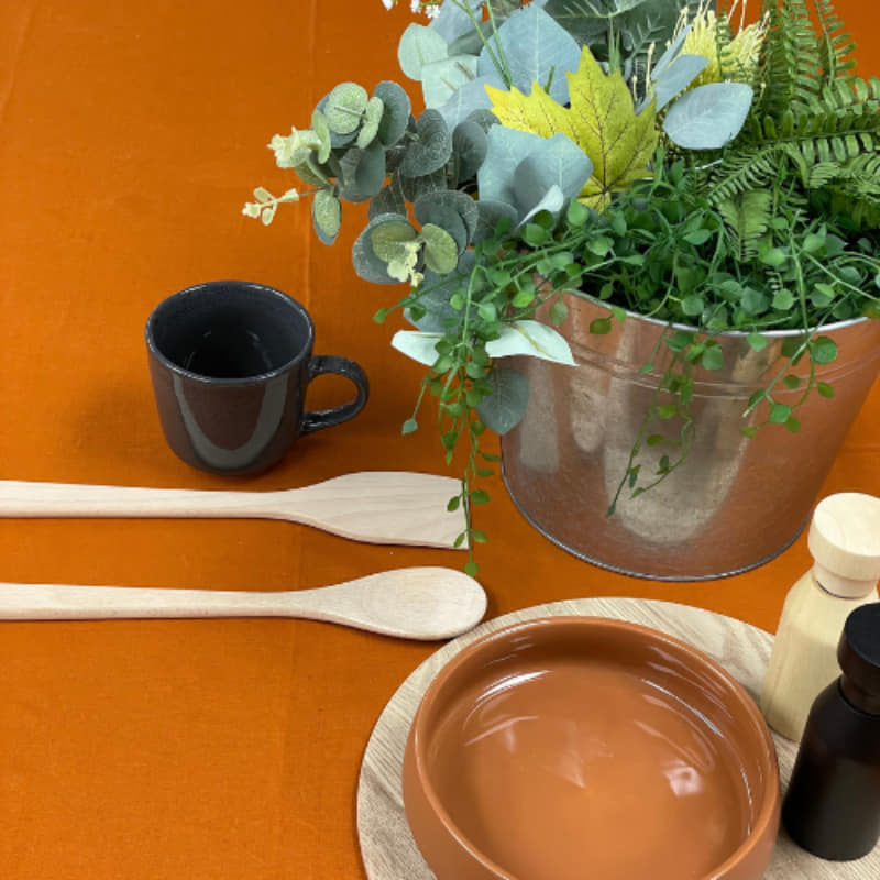 A table adorned with a pot of plants and kitchen things,  featuring a sophisticated RANS Venice Linen Terracotta Tablecloth.